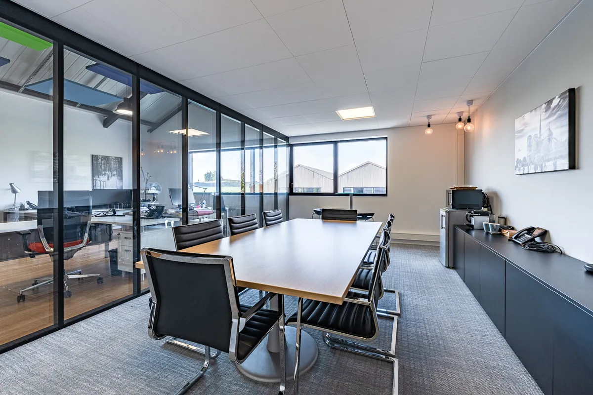 Le local aménagé lors d'une précédente occupation : salle de réunion avec table, chaises et meuble bas, cloison vitrée